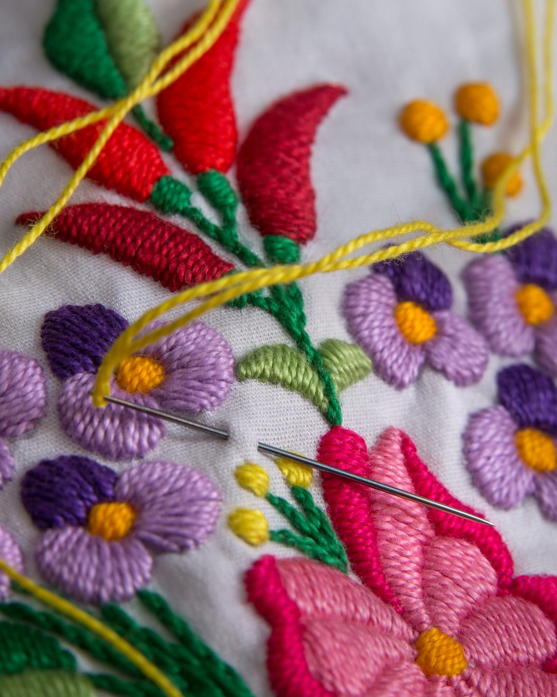 Floral embroidery in progress, a needle and yellow thread resting on white cotton