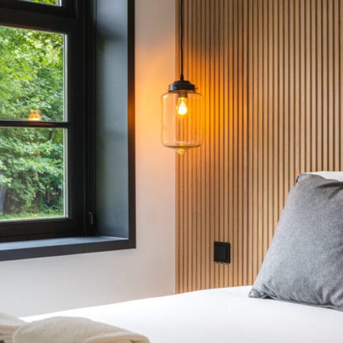 Guest room at Blooming with a white bed, wood-paneled wall and pendant lamp