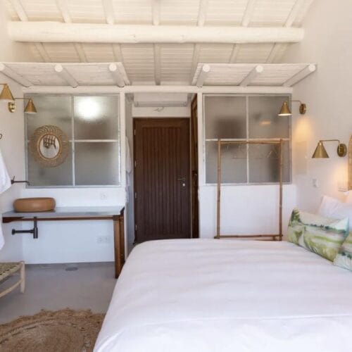 A whitewashed bedroom at Hortas do Rio, with woven wall hangings above the bed and a timber beamed ceiling