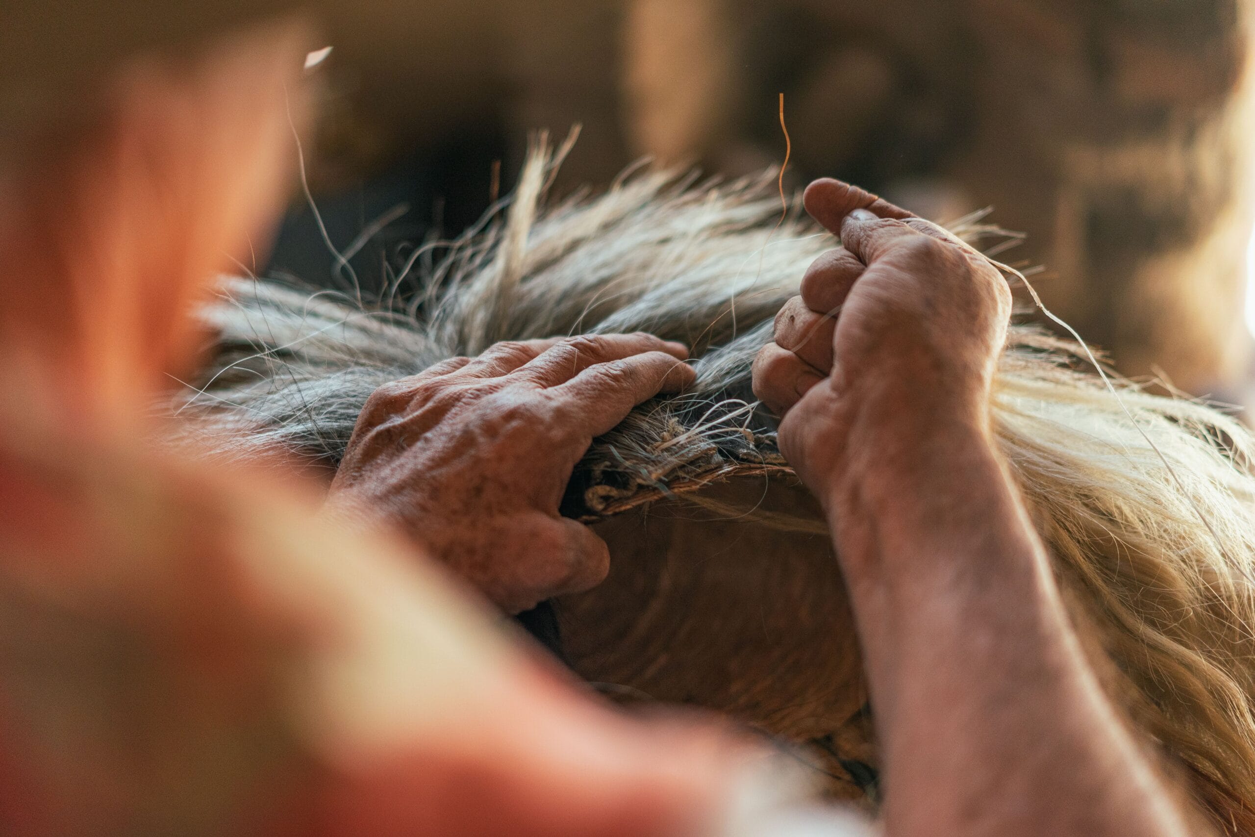 Two hands working raw wool into yarn by hand