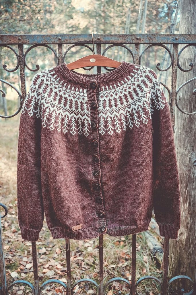 Brown wool cardigan with a white Nordic stranded yoke, hanging on a railing