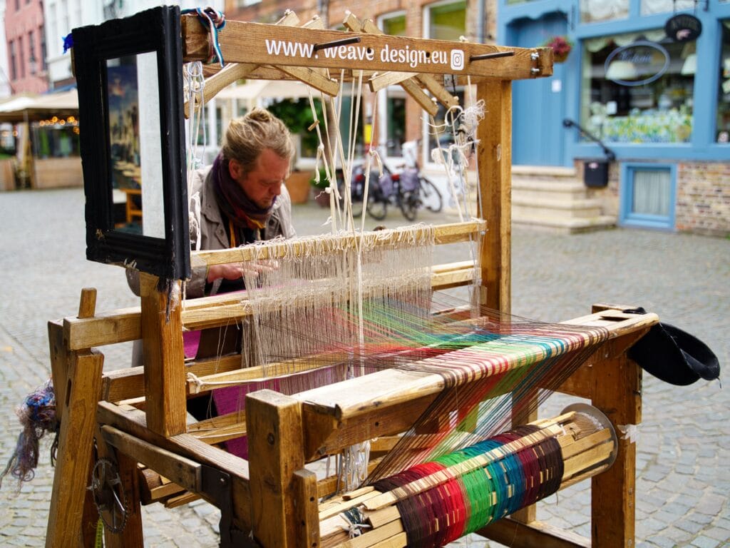 A weaver working cloth on a traditional wooden floor loom
