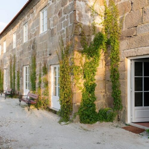 The granite facade of Casa da Granja in the Douro Valley, ivy on the walls and benches along the gravel path