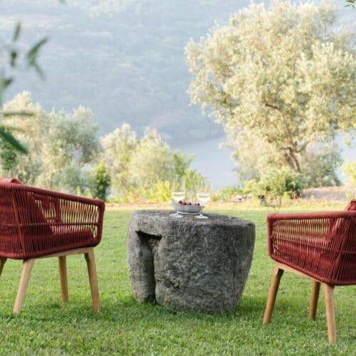 Two red chairs and a stone table in the garden at Casa da Granja, with the river Douro below