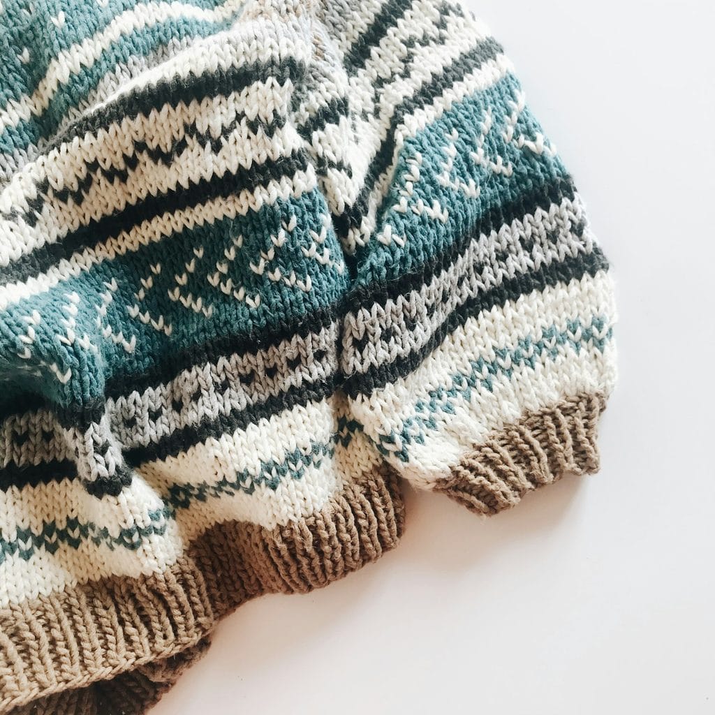 Folded sweater knitted in cream with teal and green stranded bands